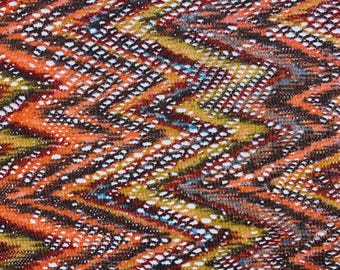 May include: Close-up of a fabric with a chevron pattern. The design features a mix of colors, including orange, brown, yellow, and white. The fabric has a textured appearance, with small white dots creating a visual contrast.