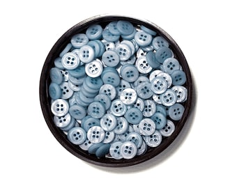 May include: A close-up of a container filled with light blue plastic buttons. The buttons have four holes and are arranged in a random pattern.