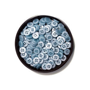 May include: A close-up of a container filled with light blue plastic buttons. The buttons have four holes and are arranged in a random pattern.