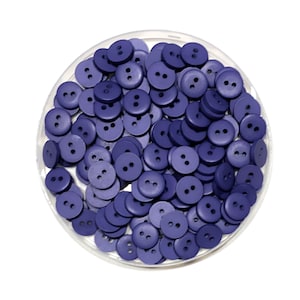 May include: A close-up view of a container filled with a large quantity of small, round, two-hole buttons. The buttons are a deep purple color.