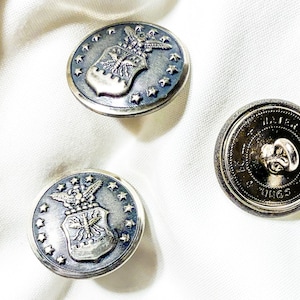May include: Three silver-toned buttons with a blue background. Two buttons feature a silver eagle and shield with stars around the edge. The third button is plain with the text "U.S. AIR FORCE" around the edge.
