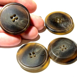 Könnte beinhalten: Vier große, runde Knöpfe mit Marmoreffekt in Braun- und Beigetönen. Jeder Knopf hat vier kleine Löcher zum Annähen. Die Knöpfe befinden sich auf weißem Hintergrund.