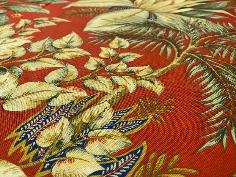 May include: Red fabric with a tropical leaf pattern. The leaves are green, yellow, and blue. The fabric has a textured surface.