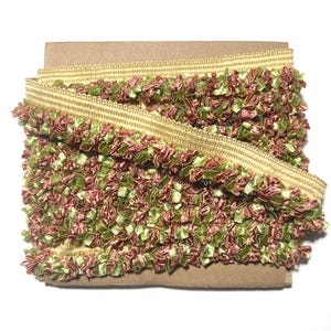 May include: A roll of decorative trim featuring a gold-colored woven base with a fringe of green and burgundy fabric. The trim is tightly wound on a cardboard spool, ready for use in craft projects.