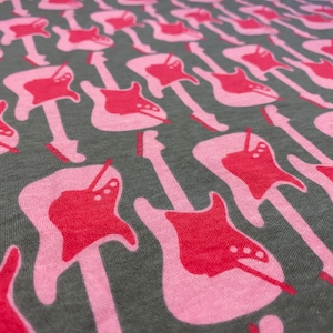 Puede incluir: Primer plano de una tela con un patrón repetido de siluetas de guitarras eléctricas rosas sobre un fondo gris oscuro.