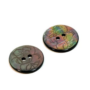 May include: Two iridescent black shell buttons with a floral design. The buttons have two holes.