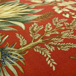 May include: Red fabric with a floral pattern featuring green and brown leaves. The fabric has a textured surface.