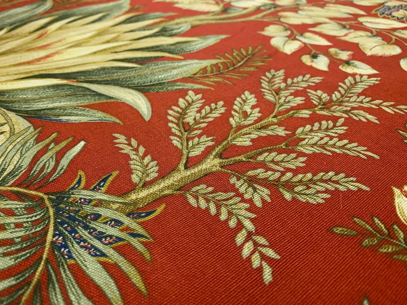 May include: Red fabric with a floral pattern featuring green and brown leaves. The fabric has a textured surface.