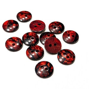 Peut inclure: Ensemble de boutons ronds avec un motif marbré rouge et noir. Chaque bouton comporte deux trous pour la couture. Les boutons sont dispersés sur une surface blanche, mettant en valeur leur design unique et leurs variations de couleurs.