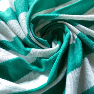 Puede incluir: Primer plano de una tela de rayas blancas y verde azulado, doblada y retorcida en forma de espiral. La tela es suave y texturizada, con un brillo sutil.