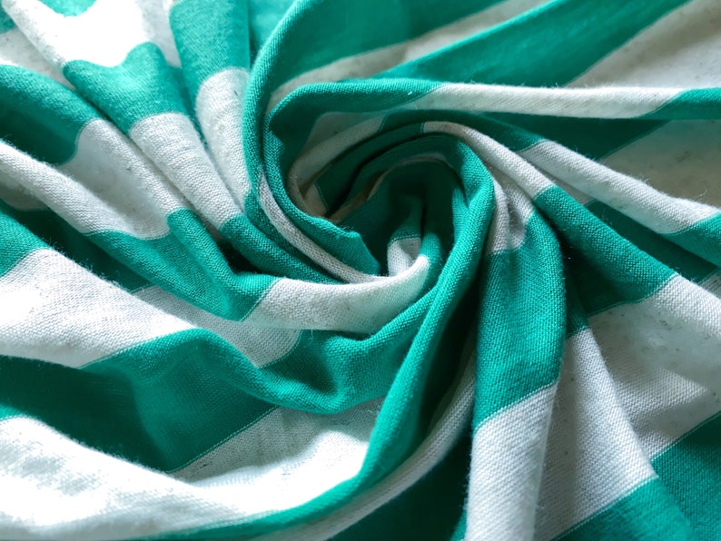 Puede incluir: Primer plano de una tela de rayas blancas y verde azulado, doblada y retorcida en forma de espiral. La tela es suave y texturizada, con un brillo sutil.