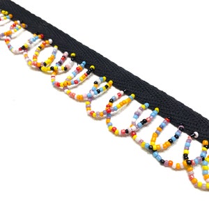 May include: Black ribbon trim with colorful beaded fringe. The fringe features a variety of small beads in yellow, orange, red, purple, blue, and white. The trim is ideal for embellishing clothing or craft projects.