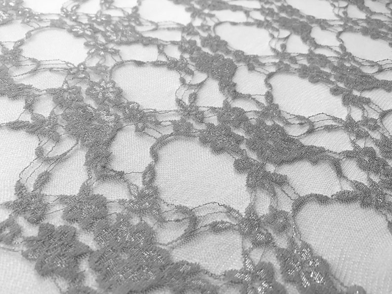 May include: Silver lace fabric with a delicate floral pattern. The lace is sheer and has a subtle shimmer.