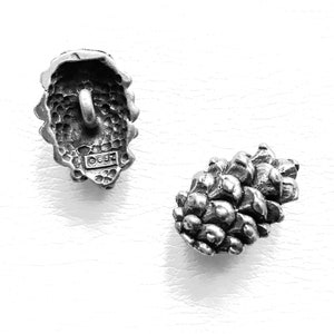 Op de afbeelding: Twee zilveren metalen knopen in de vorm van dennenappels. De knop links toont de achterkant met een kleine lus en de inscriptie "0647". De knop rechts toont de voorkant van de dennenappel.