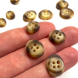 Może przedstawiać: Zbiór brązowych i kremowych guzików z czterema otworami każdy. Guziki są wykonane z marmurkowatego materiału i mają lekko uniesiony brzeg.