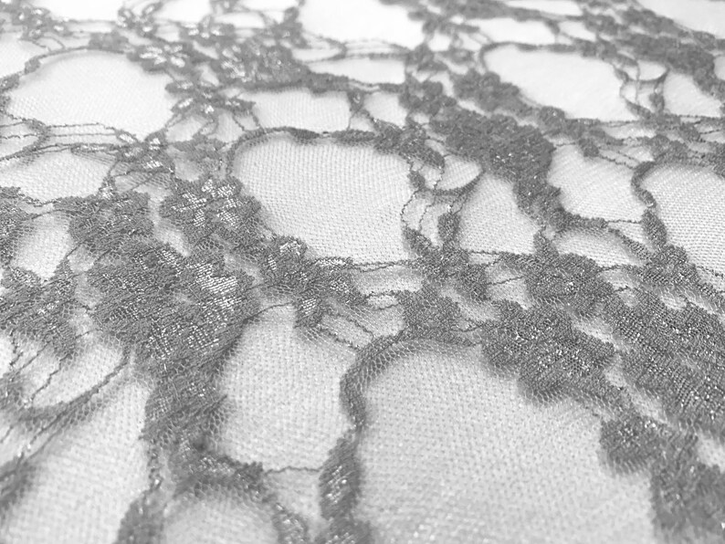 May include: Silver glitter lace fabric with a delicate floral pattern. The lace is sheer and has a soft, flowing texture.