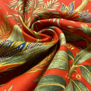 May include: Red fabric with a green, yellow, and blue floral pattern. The fabric is folded and has a textured surface.