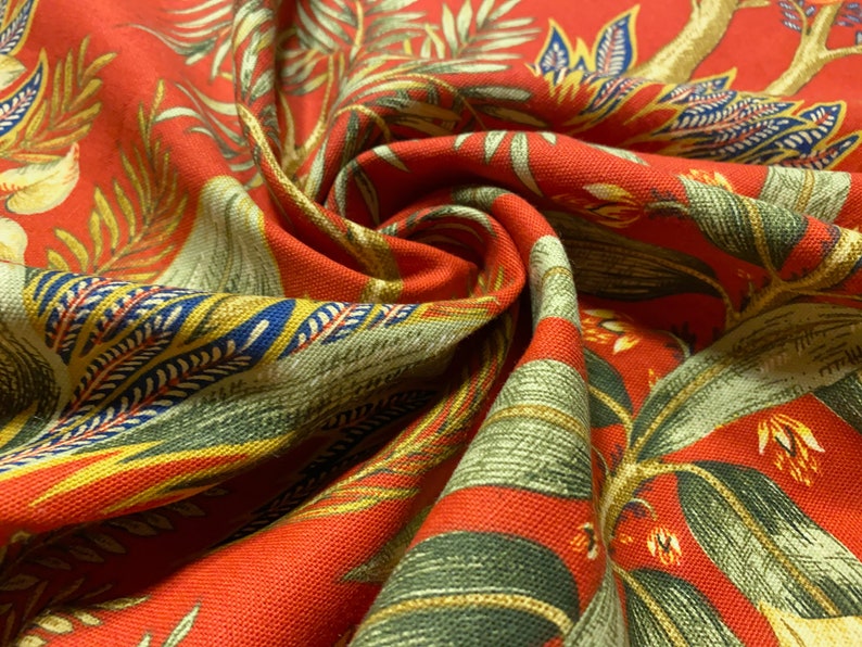 May include: Red fabric with a green, yellow, and blue floral pattern. The fabric is folded and has a textured surface.