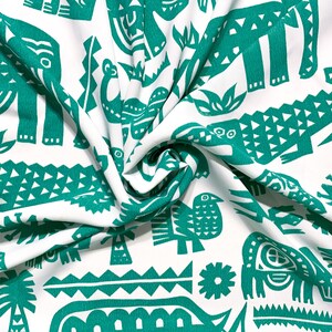 May include: White fabric with a repeating pattern of teal-colored animal and plant illustrations, including elephants, crocodiles, and birds. The fabric is folded, showing the texture and design.
