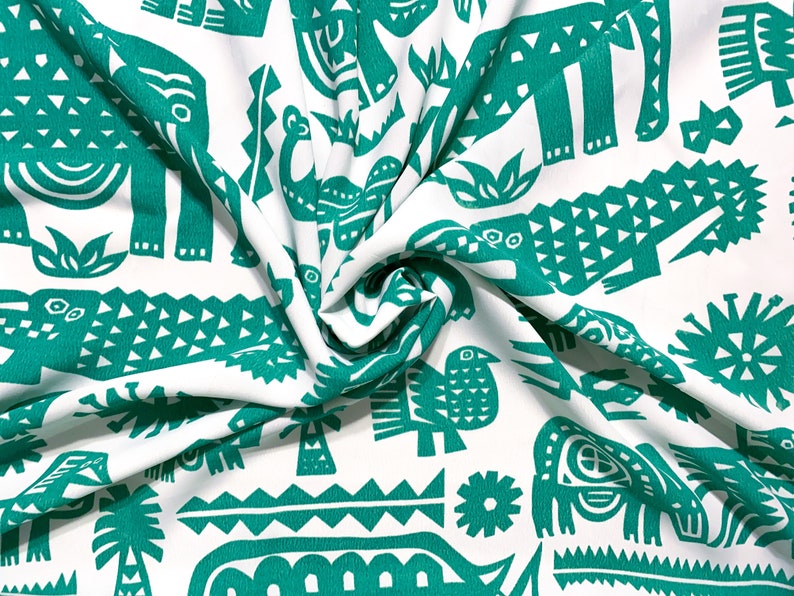 May include: White fabric with a repeating pattern of teal-colored animal and plant illustrations, including elephants, crocodiles, and birds. The fabric is folded, showing the texture and design.