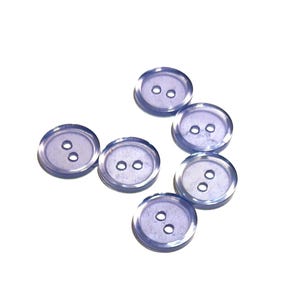 May include: Six clear, round buttons with two holes each, arranged on a white background. The buttons have a slightly translucent, lavender hue, and are made of a smooth, glossy material. These buttons are suitable for sewing and craft projects.