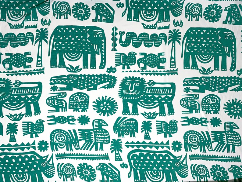 May include: White fabric with a repeating pattern of green stylized animals and plants. The design includes elephants, lions, crocodiles, birds, and palm trees. The overall aesthetic is reminiscent of a vintage safari theme.