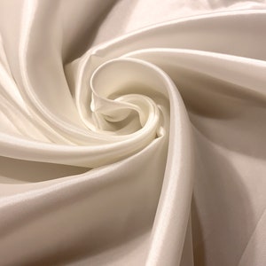 May include: Close-up of ivory-colored satin fabric, artfully arranged in swirling folds. The fabric has a subtle sheen, reflecting light and creating highlights and shadows. The image showcases the texture and drape of the material.