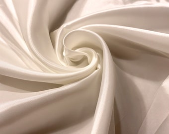 May include: Close-up of ivory-colored satin fabric, artfully arranged in swirling folds. The fabric has a subtle sheen, reflecting light and creating highlights and shadows. The image showcases the texture and drape of the material.