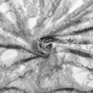 May include: A close-up of a delicate, gray lace fabric with a floral pattern. The fabric is soft and flowing, creating a romantic and elegant look.