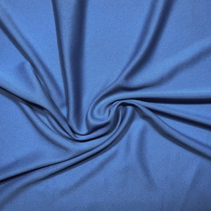 Op de afbeelding: Een close-up van een gewervelde, effen blauwe stof. De stof heeft een gladde textuur en een lichte glans, met plooien en schaduwen die diepte creëren. De kleur is een middentint blauw.