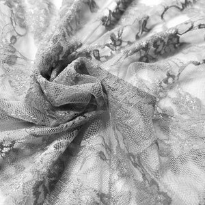 May include: A close-up of delicate white lace fabric with a floral pattern. The fabric is soft and sheer, with a delicate texture.