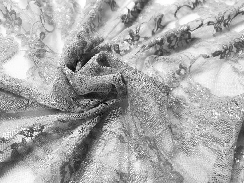 May include: A close-up of delicate white lace fabric with a floral pattern. The fabric is soft and sheer, with a delicate texture.