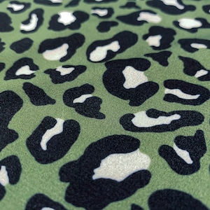 Puede incluir: Primer plano de una tela con un estampado de leopardo. El fondo es de color verde apagado, con manchas negras y blancas dispersas por la superficie. El patrón es un diseño clásico de estampado animal.