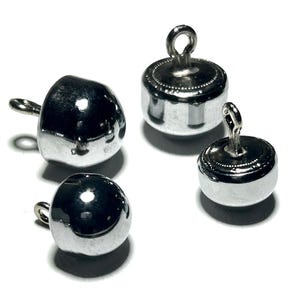 Może przedstawiać: Cztery błyszczące, srebrne metalowe koraliki z mocowaniami w pętlach. Dwa koraliki są okrągłe, a dwa mają bardziej nieregularny kształt. Koraliki znajdują się na białym tle, odbijając światło.