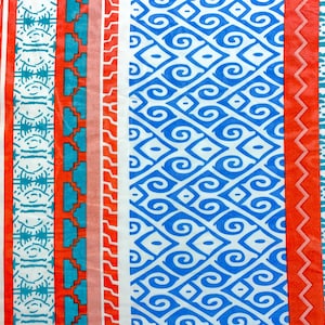 May include: A colorful fabric with a repeating pattern of blue and white swirls on a white background. The fabric is bordered by stripes of red, pink, blue, and turquoise.