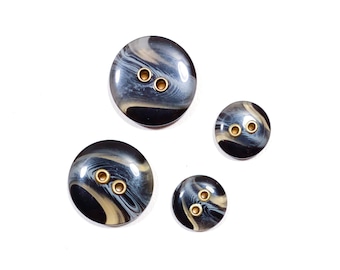 May include: Four black and white swirl patterned buttons with gold metal accents. The buttons are different sizes.