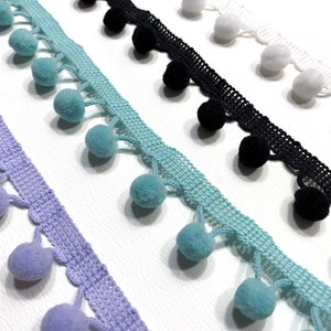 May include: Four spools of trim with pom-poms. The trim is in lavender, teal, black, and white.