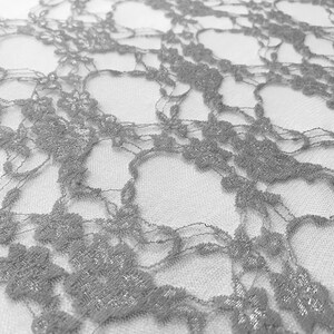 May include: Silver lace fabric with a delicate floral pattern. The lace is sheer and has a subtle shimmer.