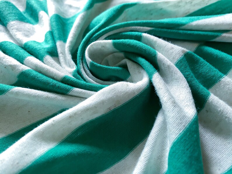Puede incluir: Primer plano de una tela de rayas blancas y verde azulado, doblada y retorcida en forma de espiral. La tela es suave y texturizada, con un brillo sutil.