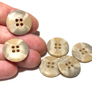 May include: A collection of round buttons with four holes each. The buttons have a marbled appearance with shades of beige and gray. The buttons are made of a smooth material and are suitable for sewing projects.