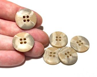 May include: A collection of round buttons with four holes each. The buttons have a marbled appearance with shades of beige and gray. The buttons are made of a smooth material and are suitable for sewing projects.
