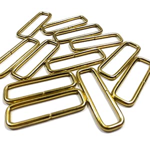 May include: A group of 10 gold-colored metal D-rings, also known as D rings or D-shaped rings. These rings are commonly used in crafting, sewing, and leatherworking projects.