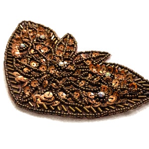 May include: A brown and gold sequined applique in the shape of a butterfly. The applique is made of small, round sequins and beads.