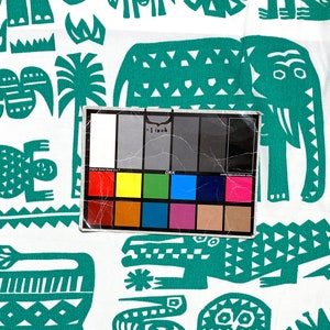 May include: White fabric with a repeating pattern of teal-colored stylized animals and plants. The design includes elephants, crocodiles, and other creatures. A color calibration card is in the foreground.