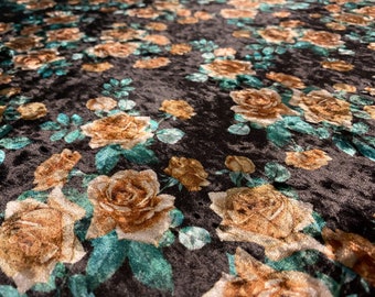May include: Close-up of a black fabric with a floral pattern. The design features large, detailed roses in shades of gold and brown, with teal green leaves. The fabric has a velvety texture, creating a rich and luxurious appearance.