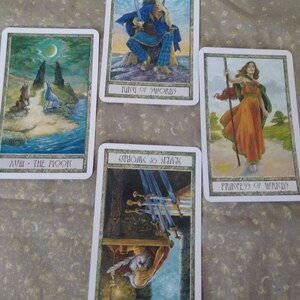 May include: Four tarot cards, featuring illustrations of a wolf howling at the moon, a king sitting on a throne, a woman holding a staff, and a man with swords. The cards are labeled "XVIII - The Moon", "King of Swords", "Princess of Wands", and "Seven of Swords".