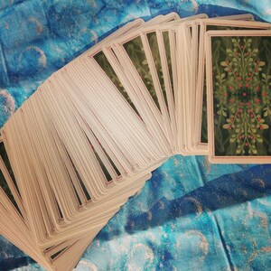 May include: A deck of tarot cards with a green and red floral design on the back of the cards. The cards are fanned out in a semi-circle.