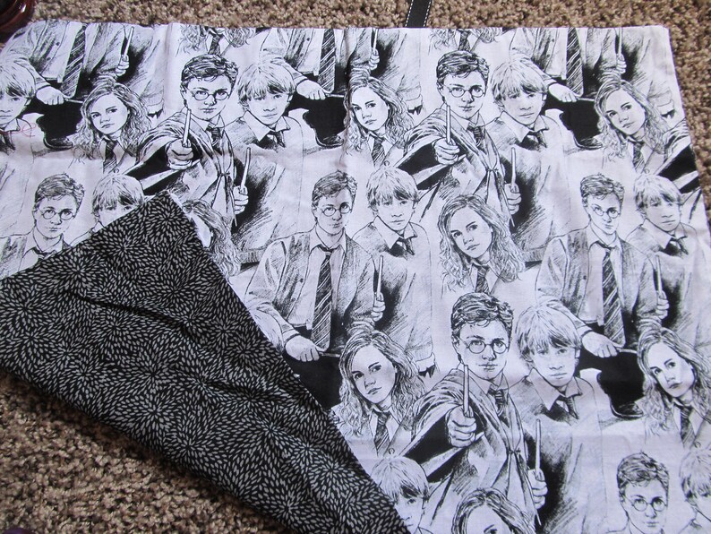 May include: Black and white fabric with a repeating pattern of Harry Potter characters. The characters are drawn in a cartoon style and include Harry Potter, Ron Weasley, and Hermione Granger.
