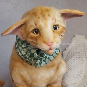 Realistic soft stuffed orange tabby Oriental breed cat toy has yellow taxidermy eyes, pink colored polymer clay paws, white translucent polymer clay claws, and artificial whiskers. The cat  has a green scarf with a diamond pattern. Perfect for collectors, gifts, memorial pet, and home decor.