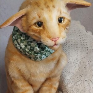 Realistic soft stuffed orange tabby Oriental breed cat toy has yellow taxidermy eyes, pink colored polymer clay paws, white translucent polymer clay claws, and artificial whiskers. The cat  has a green scarf with a diamond pattern. Perfect for collectors, gifts, memorial pet, and home decor.